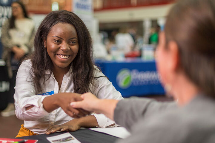 A Black student shakes hands with a recruiter at a job fair on campus.